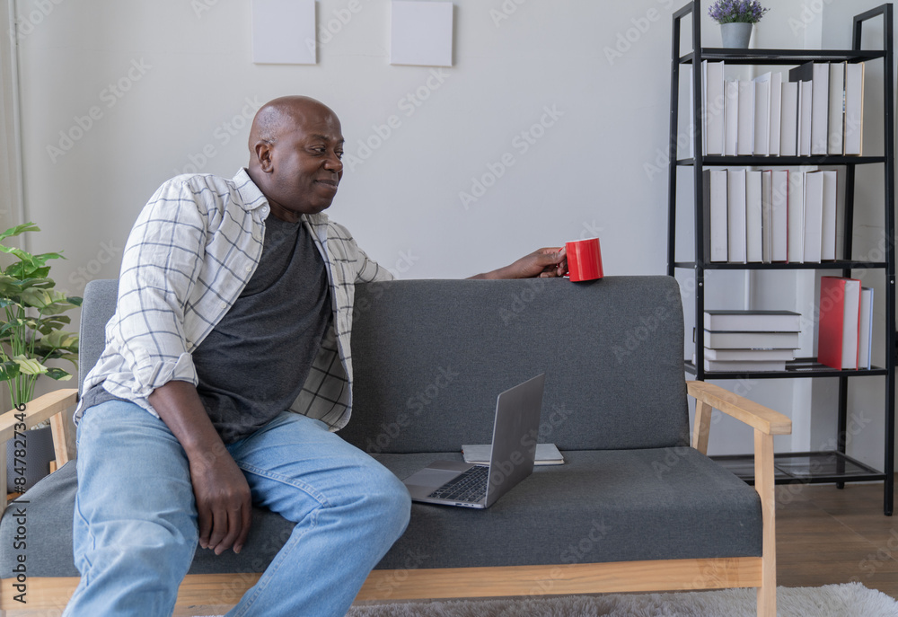 Fototapeta premium Portrait of happy African American small business owner. Millennial black smiling, sitting and using the laptop, and holding a cup of coffee work in modern office.
