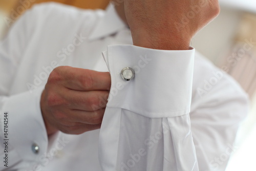 Fotografia Elegant businessman is fastening a cufflink on his white shirt getting ready for