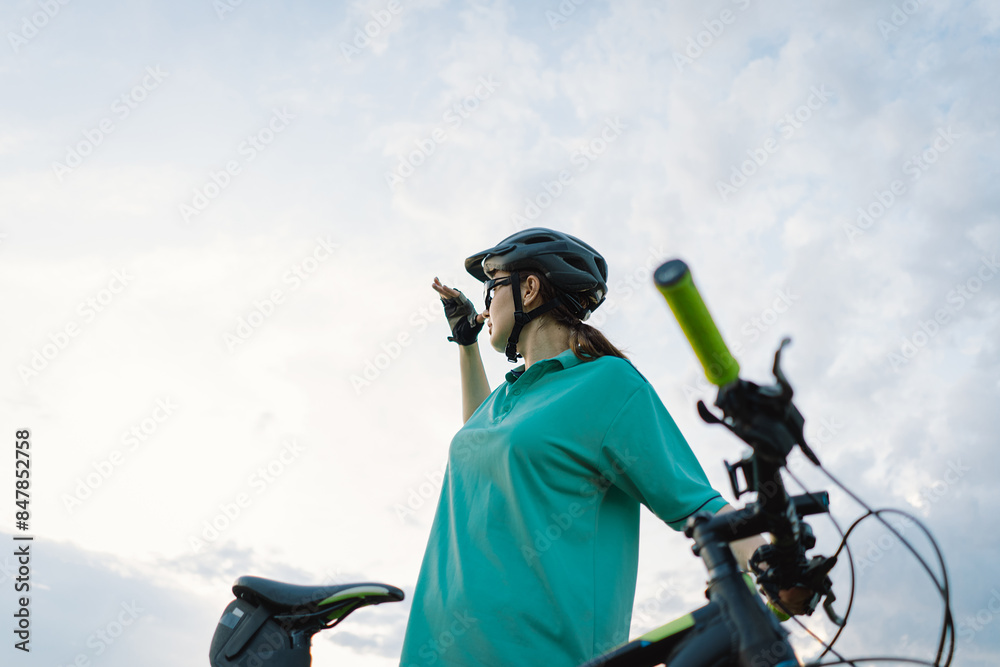 Obraz premium A young person, wearing a helmet and a shirt, looks up at the sky while riding a bicycle. The cyclists hand is on the handlebars, and the bikes seat is visible in the foreground.