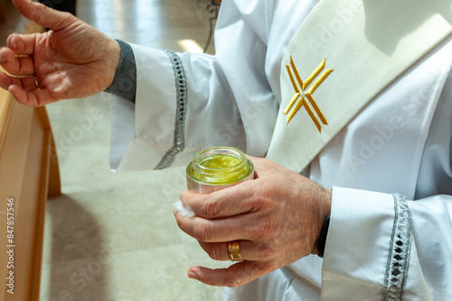 Religious ceremony, priest in white robe holding jar of chrism oil