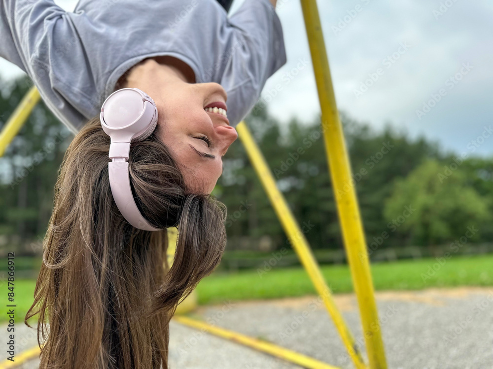 Obraz premium Pretty young woman hanging upside down with her headphones on, celebrating love and life, enjoying summer and autumn, healthy lifestyle concept 