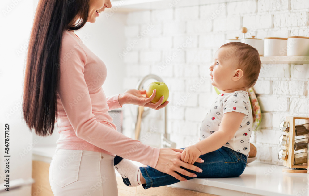 A woman is gently holding an apple towards a baby, who is reaching out to touch the fruit. The baby appears curious and excited, while the woman seems caring and affectionate. A woman is gently holding an apple towards a baby, who is reaching out to touch the fruit. The baby appears curious and excited, while the woman seems caring and affectionate.