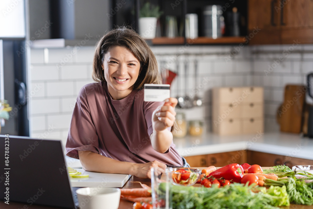 A young cheerful woman is buying groceries by ordering them online and paying for them with a card A young cheerful woman is buying groceries by ordering them online and paying for them with a card