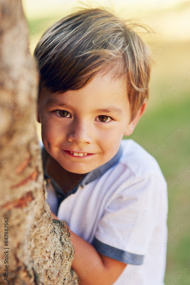 Boy, hide and happy by tree for portrait in park for games, adventure and outdoor for playing in summer. Child, nature and shy smile in forest for holiday, vacation and freedom for growth in Canada Boy, hide and happy by tree for portrait in park for games, adventure and outdoor for playing in summer. Child, nature and shy smile in forest for holiday, vacation and freedom for growth in Canada
