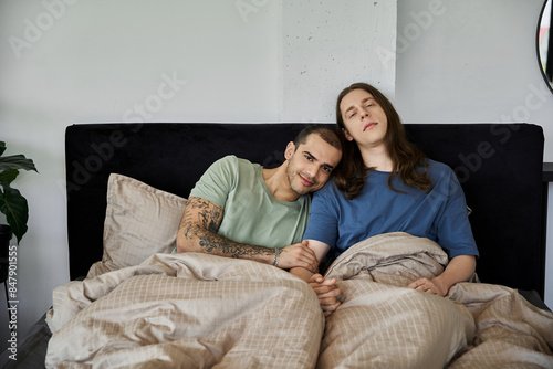 A young gay couple snuggles in bed together, enjoying a moment of intimacy and connection.