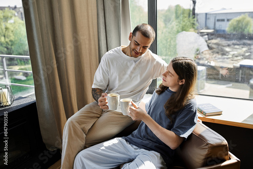 A young gay couple enjoys a morning coffee together in their modern home, filled with natural light.
