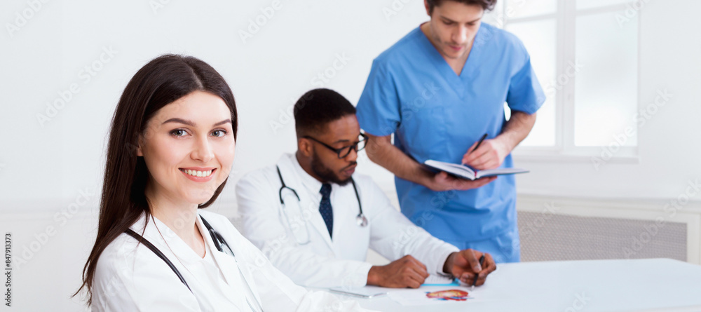 Team of doctors having meeting in medical office, woman looking at camera Team of doctors having meeting in medical office, woman looking at camera