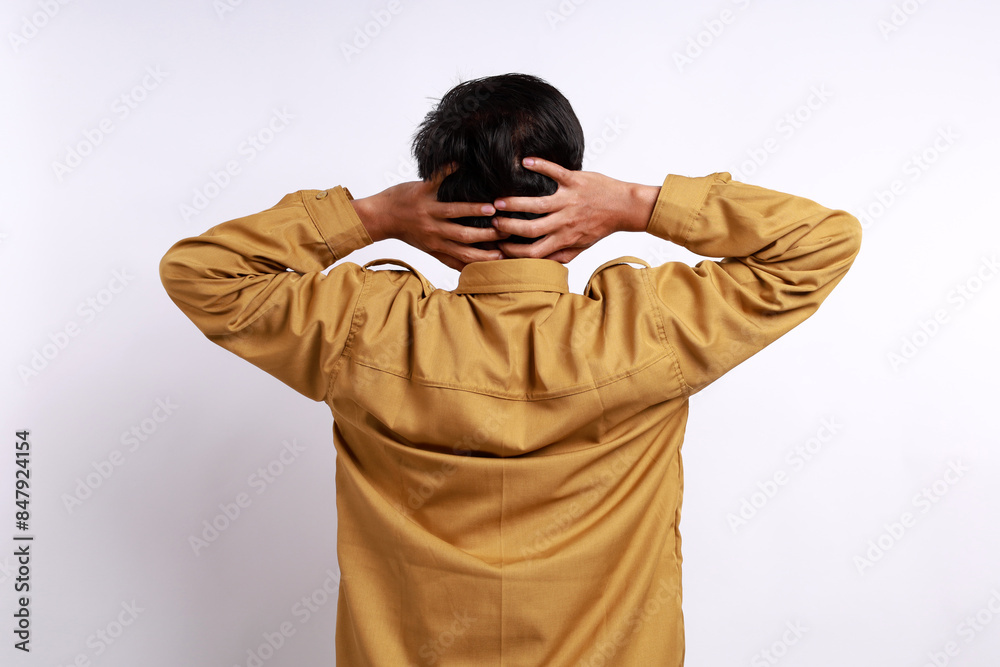 A portrait of an Asian Indonesian government employees, photographed from behind, experiencing a headache and holding his head. Isolated against a white background A portrait of an Asian Indonesian government employees, photographed from behind, experiencing a headache and holding his head. Isolated against a white background