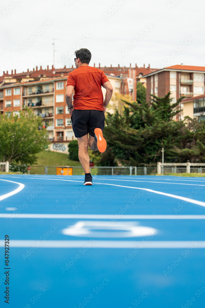 Fototapeta premium vertical Rear View of Male Runner Jogging on Blue Athletic Track