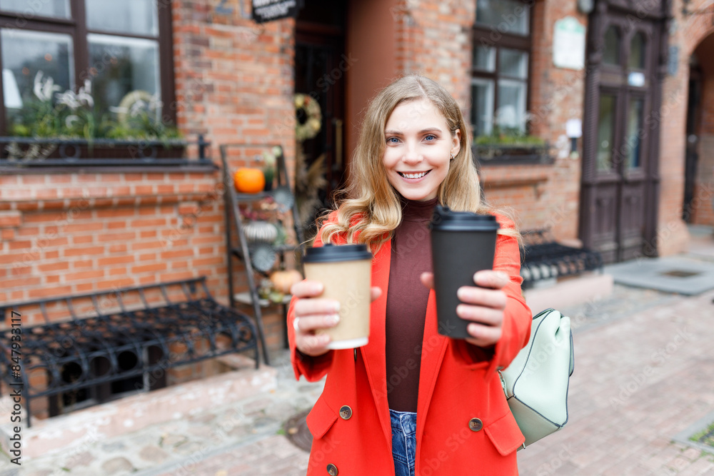 Fototapeta premium Cheerful young woman wearing red coat walking with coffee cup