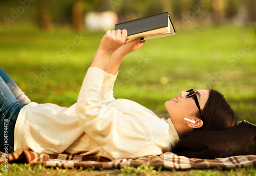 Korean woman is laying on the ground, engrossed in a book she is reading. She is surrounded by a peaceful environment, completely focused on the story unfolding in her hands. photo