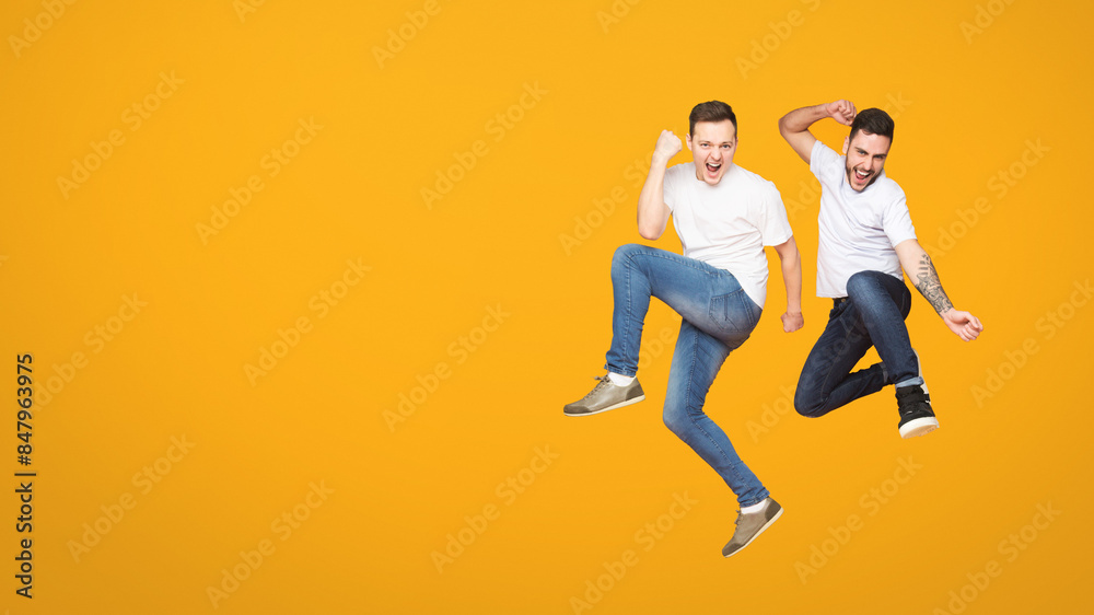 Duo of european men captured mid-jump against orange backdrop, encapsulating the essence of friendship and camaraderie among mates Duo of european men captured mid-jump against orange backdrop, encapsulating the essence of friendship and camaraderie among mates