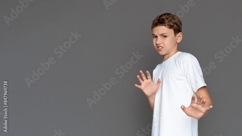 A teenager in a white shirt stands with a defensive posture, expressing caution or fear, against a grey, isolated background. His expression suggests hesitation or concern