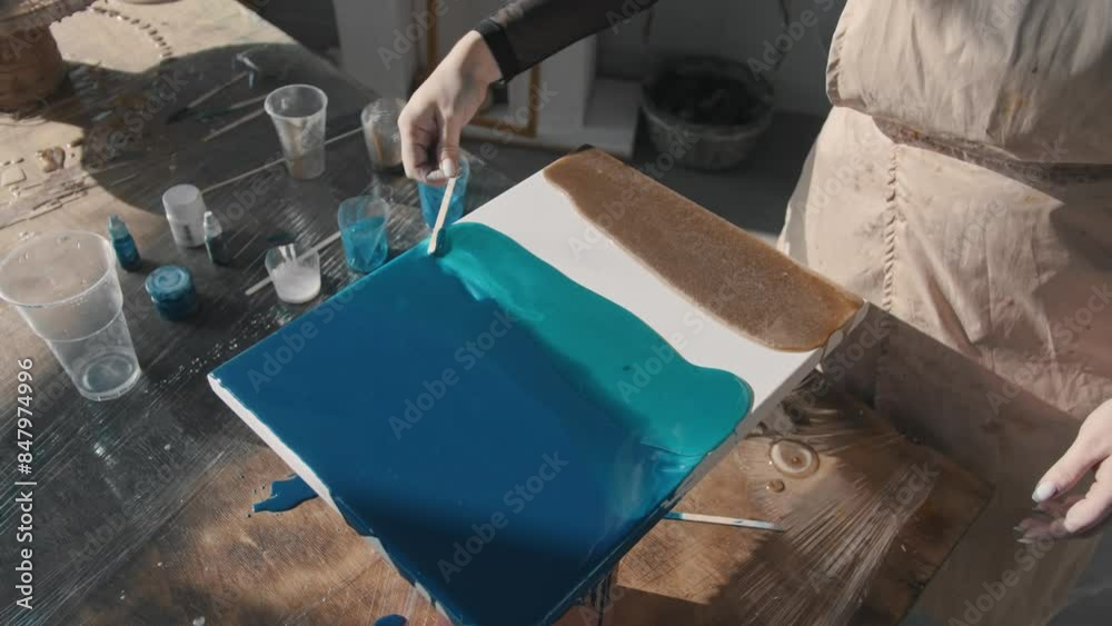 Artist creates her paintings using an unusual technique that involves epoxy resin. Instead of using a brush, she applies the resin to the canvas using a wooden stick. Close up. Slow motion
