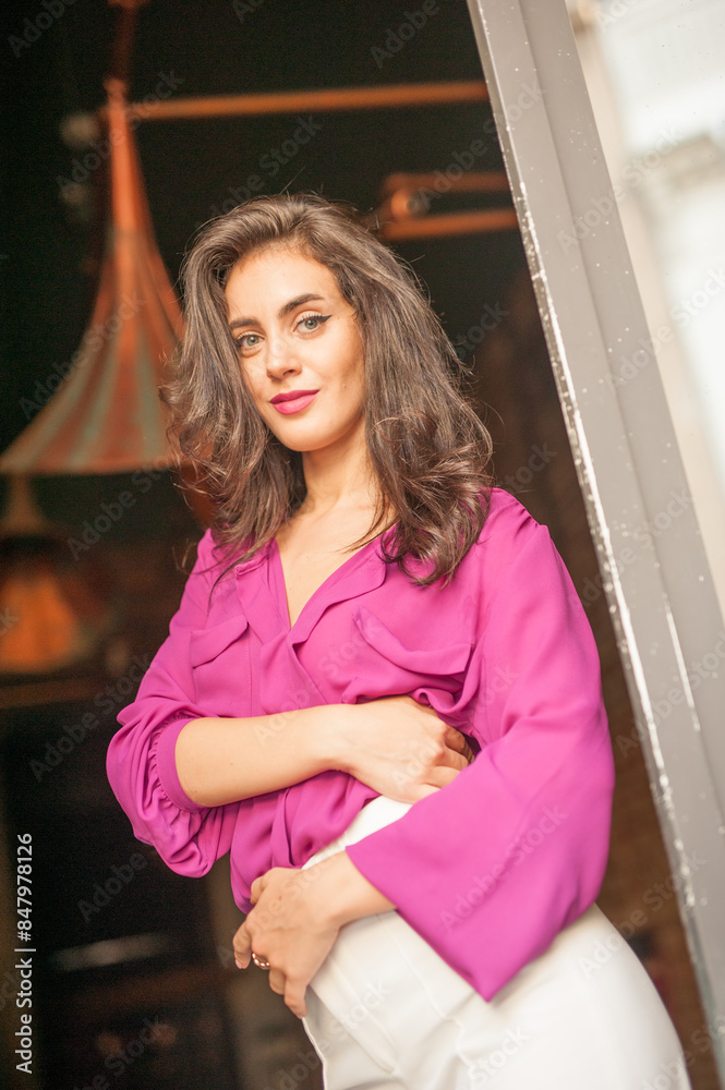 Beautiful young brunette woman in a purple blouse and white pants posing outdoor. Portrait of a beautiful young brunette woman with long hair posing fashion