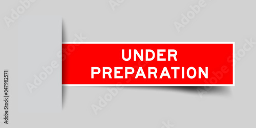 Red color square label sticker with word under preparation that inserted in gray background