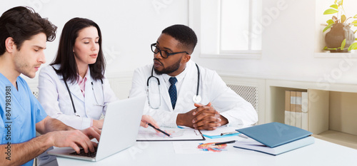 Young medical team discussing reports, using laptop in meeting room photo