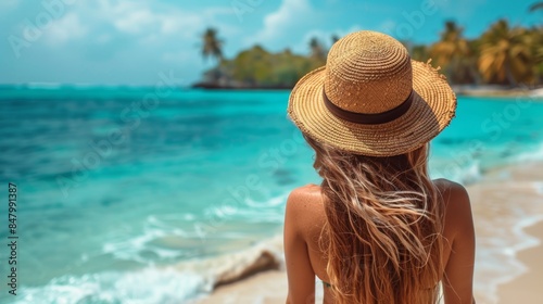 Woman in a straw hat admires the turquoise ocean waves while enjoying a relaxing beach vacation