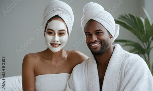 Beauty portrait of man and woman wearing bathrobe and towels on heads and facial mask against bathroom background. Headshot of adult couple after spa treatment. Skincare routine, cosmetology concept