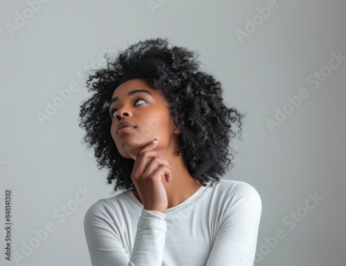 A woman looks up in thought, with a plain white background, representing stock artificial intelligence. © Mark