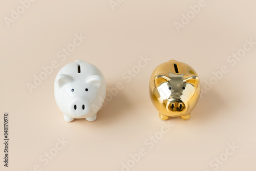 One white and one gold coloured piggy bank on cream coloured background.