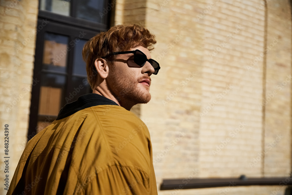 Red-haired man exudes debonair style in a yellow jacket and black sunglasses while walking in the city. Red-haired man exudes debonair style in a yellow jacket and black sunglasses while walking in the city.