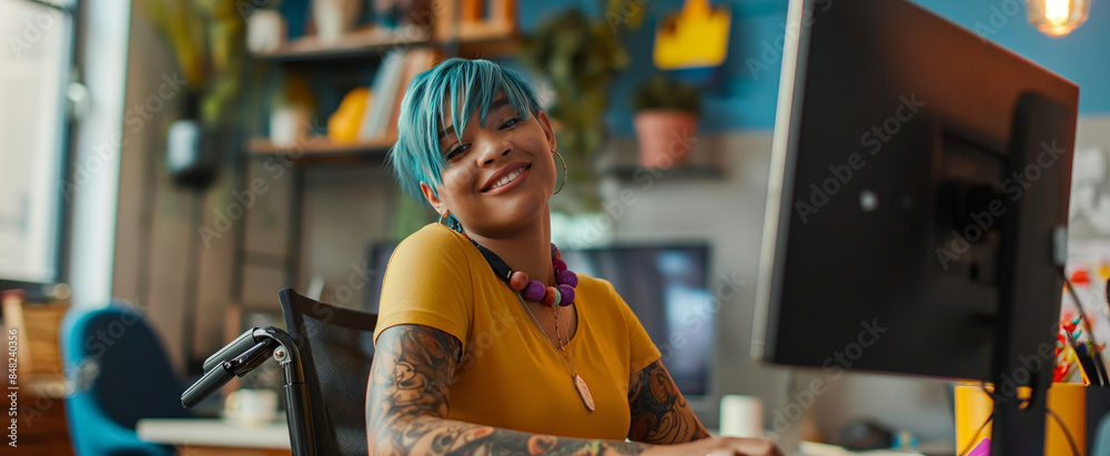 Inclusive photo of female employee with blue hair sitting in a wheelchair in diverse & accessible dei workplace. Happy remote worker at computer. Pride month business marketing