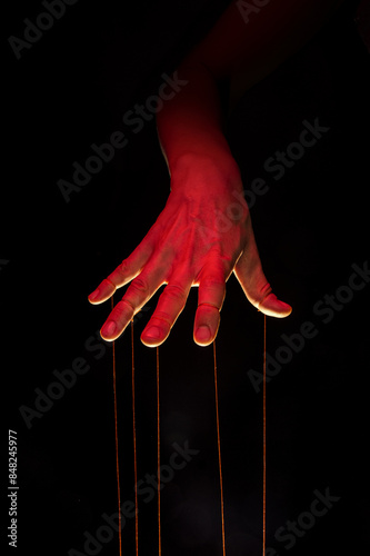 A puppeteer's hand with strings on each finger on black background.