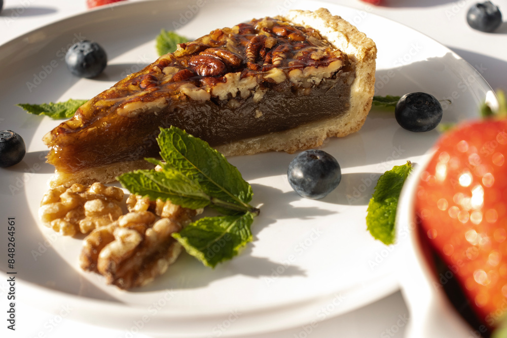 Pecan pie on a plate. Blueberries, nuts and mint leaves for dessert decoration. A yellow plate on a white background close-up. Pecan pie on a plate. Blueberries, nuts and mint leaves for dessert decoration. A yellow plate on a white background close-up.