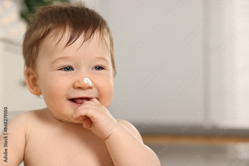 Cute little baby with moisturizing cream on face indoors, space for text Cute little baby with moisturizing cream on face indoors, space for text