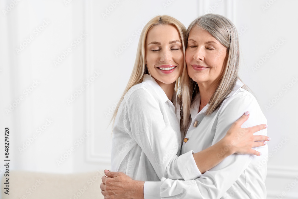 Family portrait of young woman and her mother near white wall. Space for text Family portrait of young woman and her mother near white wall. Space for text