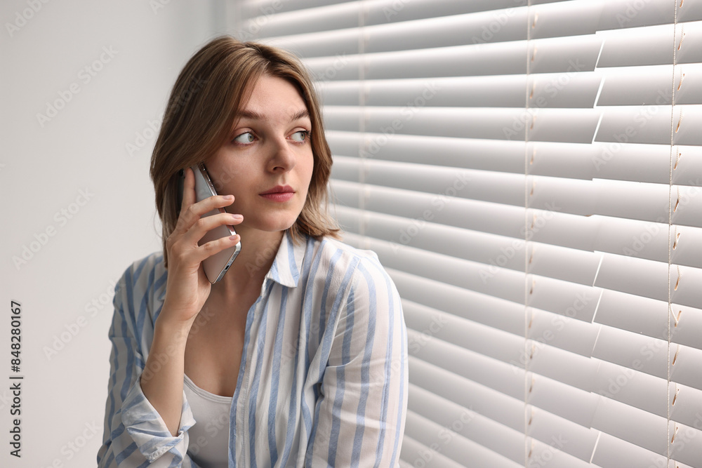 Woman talking on phone near window blinds at home, space for text Woman talking on phone near window blinds at home, space for text
