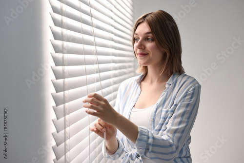 Young woman adjusting window blinds at home Free Download Young woman adjusting window blinds at home - GFXLoad