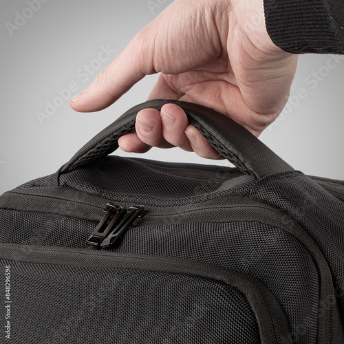 Sturdy black backpack designed with multiple zippered compartments and adjustable straps against grey background. Concept of  convenient stylish accessory for business trips and travel photo