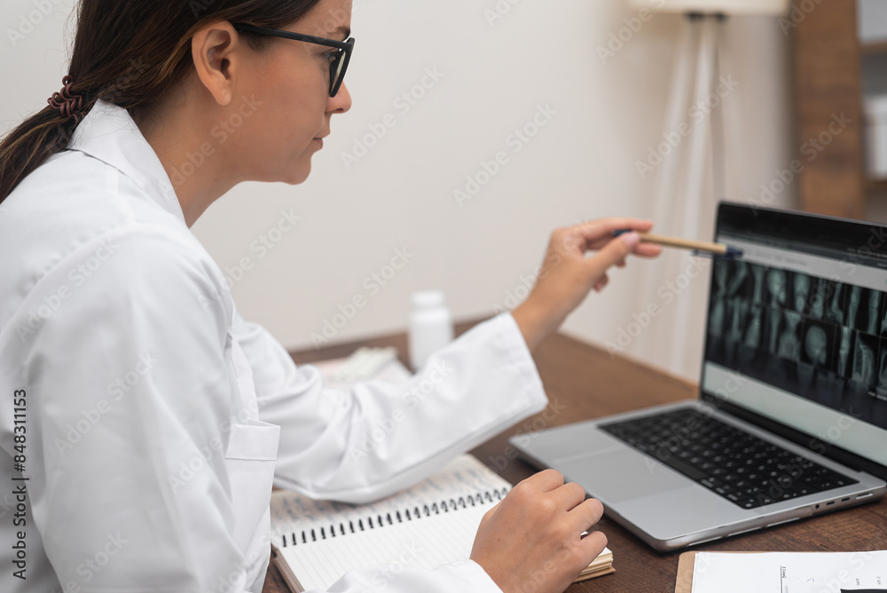 X-ray Diagnosis: Focused and analytical, a young doctor in glasses analyzes X-ray images displayed on a laptop. 