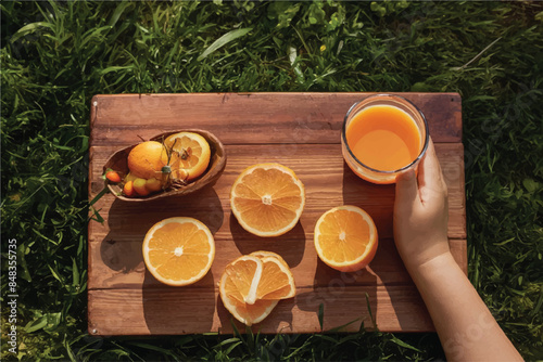 Fresh orange juice in glass beaker, slices of sliced oranges and basket on background of spring green nature with sunbeams. Vitamins and fruits. Healthy lifestyle. Spring background with orange juic