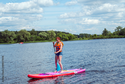 Water sports on river. Summer travel destination. Happy Caucasian woman in life vest paddling on sap board in the lake