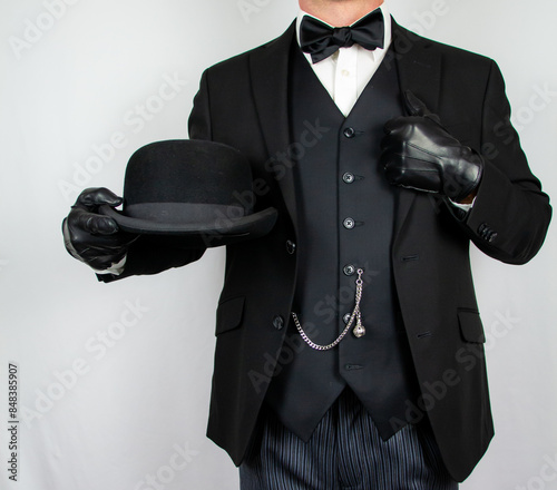 Portrait of Gentleman in Dark Suit and Leather Gloves Holding Bowler Hat. Classic British Butler Standing at Attention.
