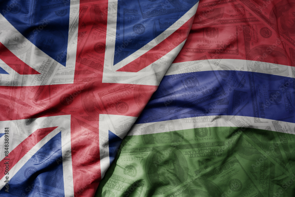 big waving colorful flag of gambia and national flag of great britain on the dollar money background. finance concept. big waving colorful flag of gambia and national flag of great britain on the dollar money background. finance concept.