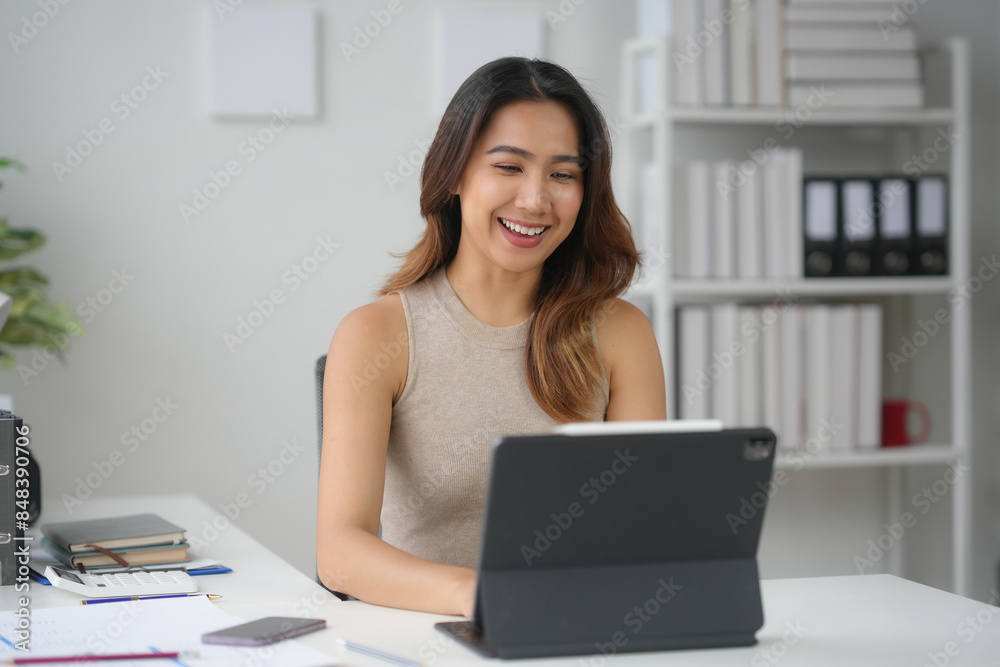 Smiling woman working on a tablet at a modern office desk, surrounded by books, papers, and office supplies. Smiling woman working on a tablet at a modern office desk, surrounded by books, papers, and office supplies.