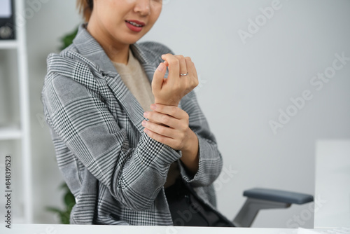 Woman experiencing wrist pain sitting at office desk, potential symptom of repetitive strain injury due to continuous computer usage.