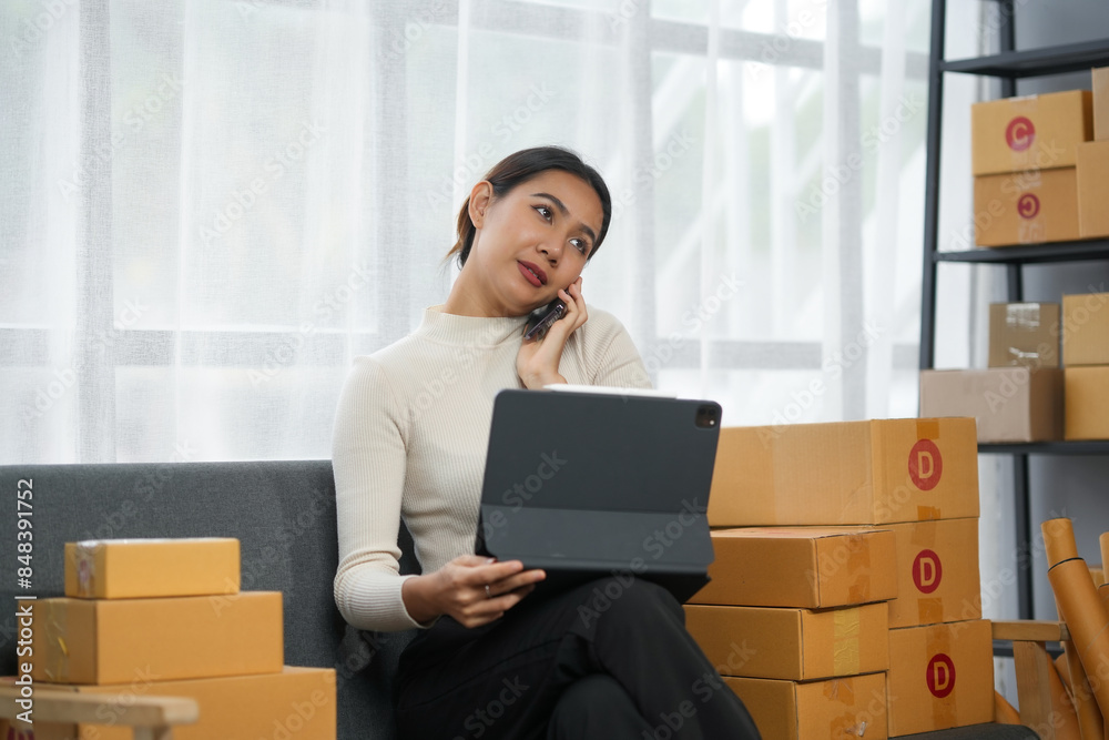 Woman on phone working with tablet surrounded by boxes in a modern home office. E-commerce business concept. Woman on phone working with tablet surrounded by boxes in a modern home office. E-commerce business concept.