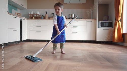 the child baby washes the floors. happy family kid dream concept. child son washes the floors with a mop in the kitchen in an apron helps mom. mom asked the child son to mop the floors indoors