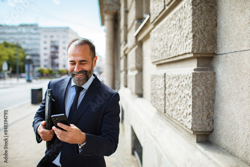 Smiling businessman in a suit holding a smartphone in city