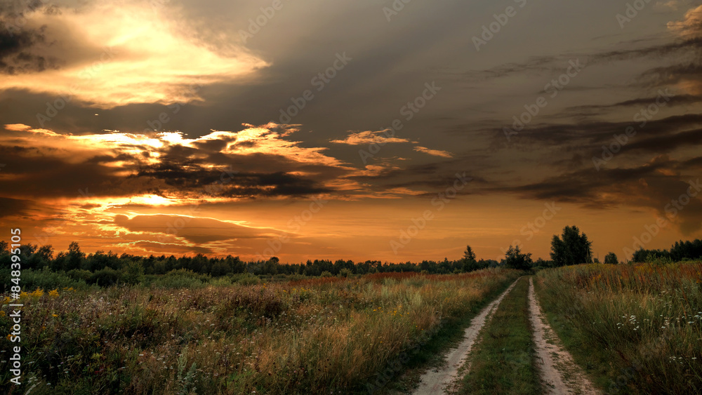 Obraz premium Rural road in a field against the backdrop of a summer sunset.
