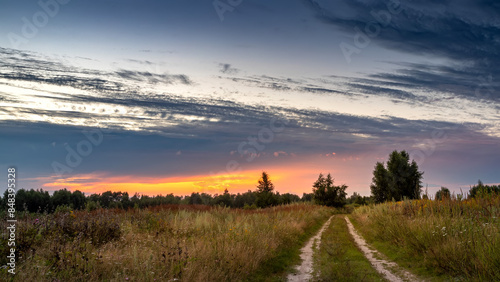 Rural road in a field against the backdrop of a summer sunset.