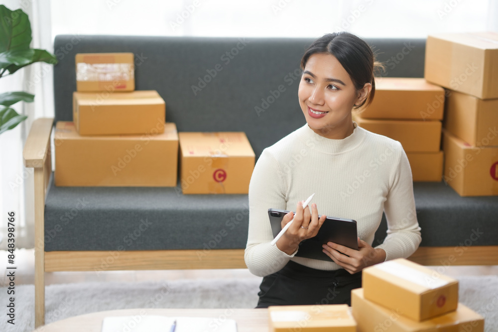 Young woman working at home with boxes, writing in a notebook, running her online business for shipping products. Entrepreneurship concept. Young woman working at home with boxes, writing in a notebook, running her online business for shipping products. Entrepreneurship concept.