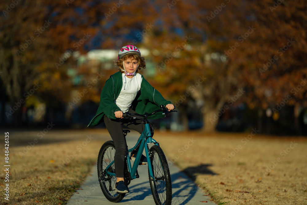 Naklejka premium Cute kid boy riding a bike in the autumn park. Little kid boy in warm clothes in autumn park driving a bicycle. Active child cycling on sunny fall day in nature. Autumn leisure with kids.