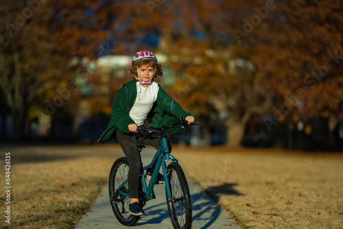 Cute kid boy riding a bike in the autumn park. Little kid boy in warm clothes in autumn park driving a bicycle. Active child cycling on sunny fall day in nature. Autumn leisure with kids.