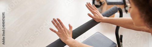 A sporty woman gracefully stretches her arms on a bar during a Pilates lesson.